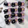 Muestra de 12 tarjetas de cartón con colitas elásticas negras para el cabello distribuidas en filas sobre fondo blanco.