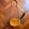 Cartera bandolera color mostaza con correa de cadena sobre piso de madera