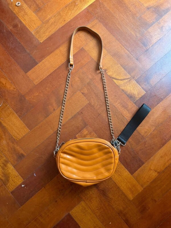 Cartera bandolera color mostaza con correa de cadena sobre piso de madera